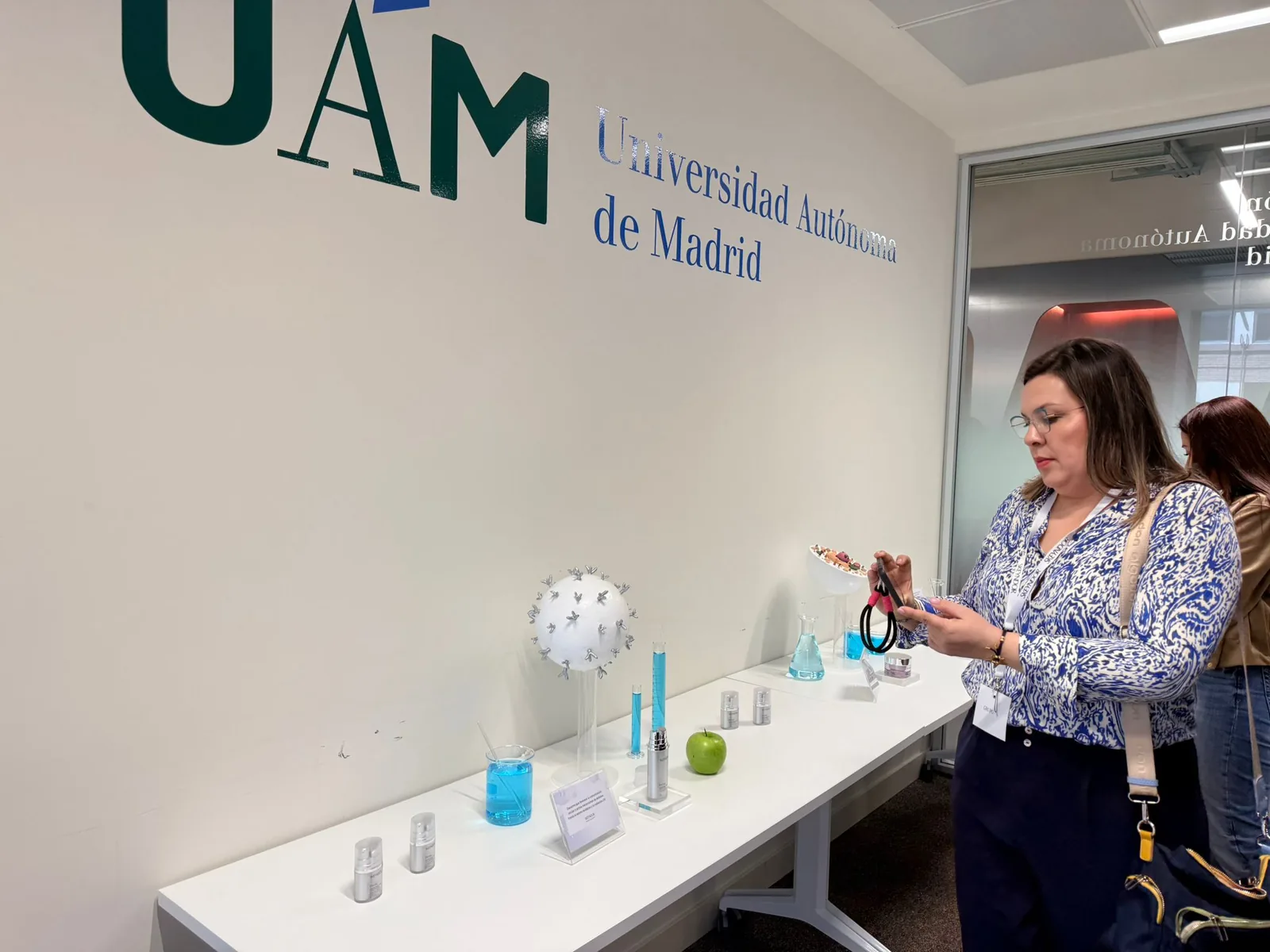Mesa de exposición con matraces de laboratorio, modelo molecular y muestras cosméticas en la Universidad Autónoma de Madrid